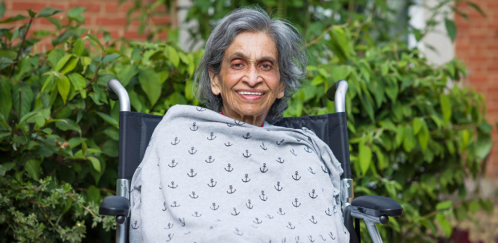 A elderly lady sitting outside in her wheelchair, smiling.